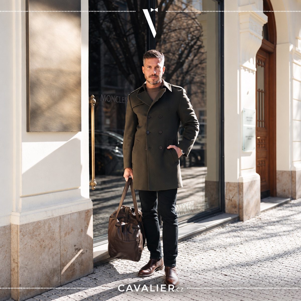 Pánský olivový kabát na míru v elegantním smart casual outfitu s koženou taškou.