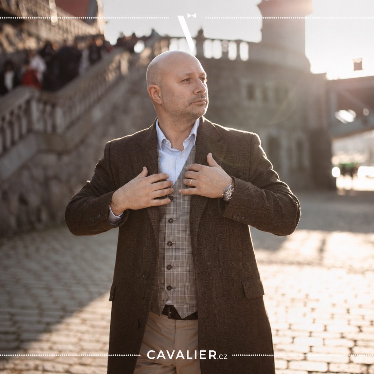 Detail hnědého kabátu na míru, kožených hodinek a pánského smart casual outfitu.