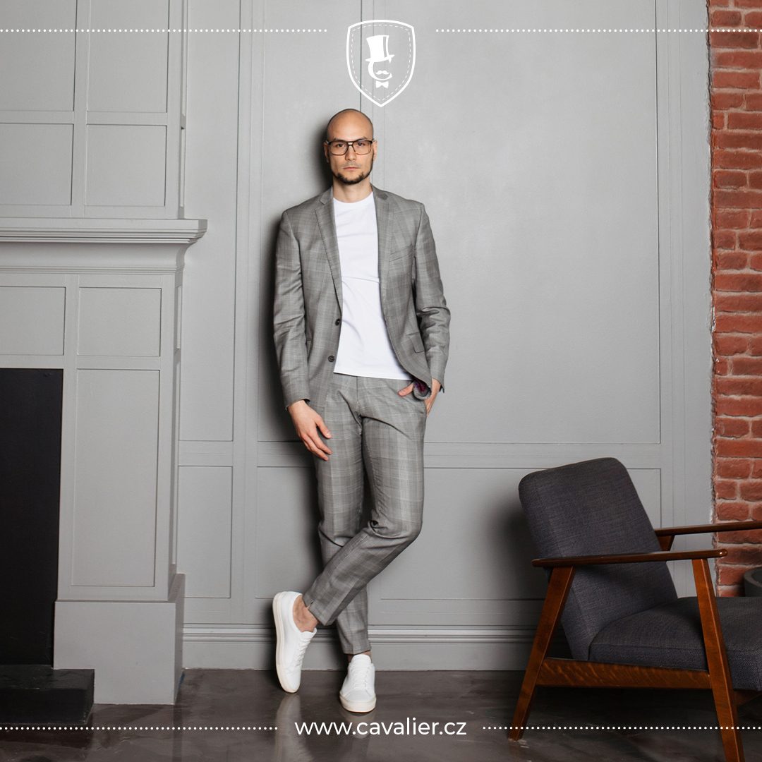 Muž v šedém kostkovaném obleku na míru Cavalier oblečeném s bílým tričkem jako ukázka triku pro uvolněný neformální styling