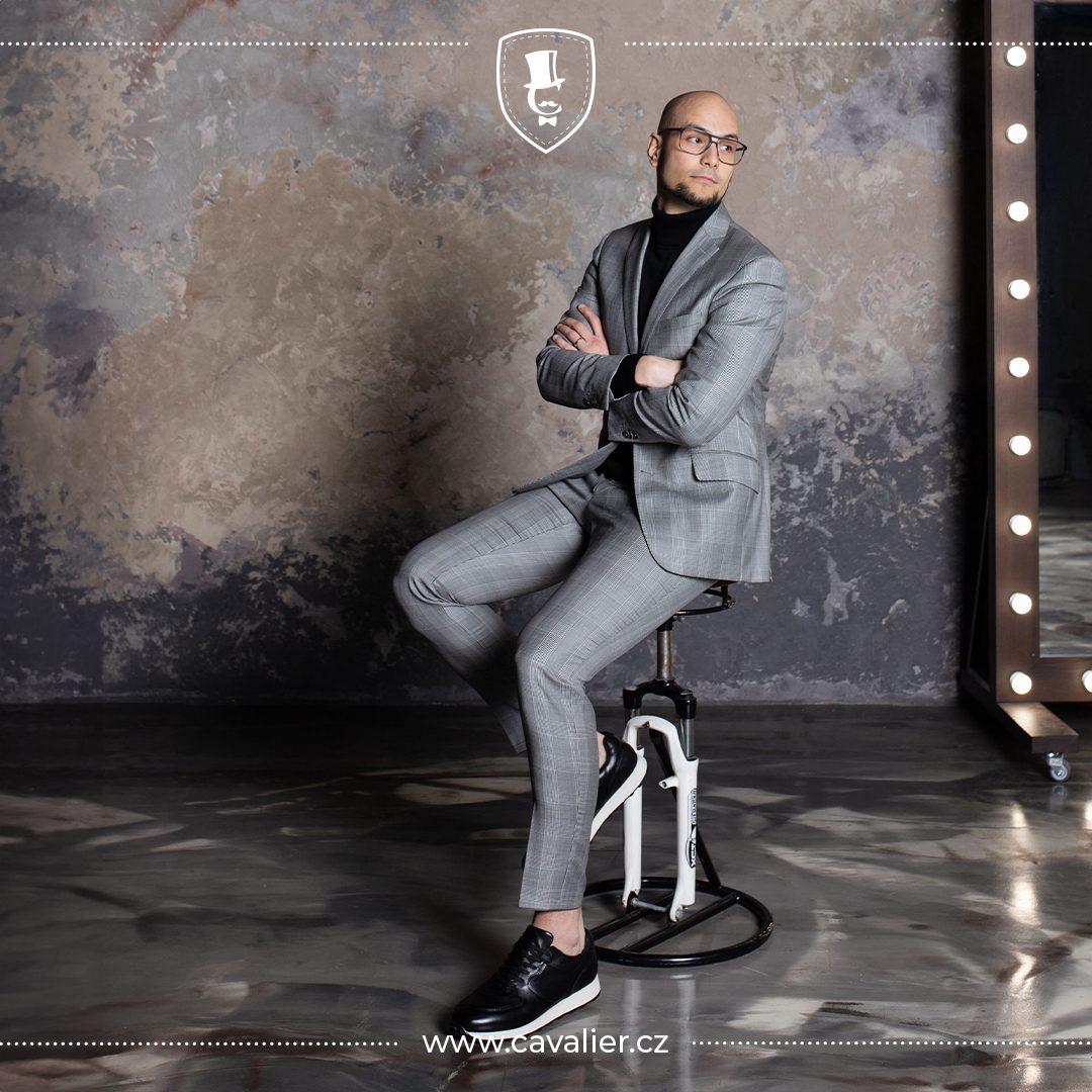 Muž v šedém kostkovaném obleku na míru Cavalier zkombinovaném s černým rolákem a teniskami jako trik pro ležérní smart casual vzhled