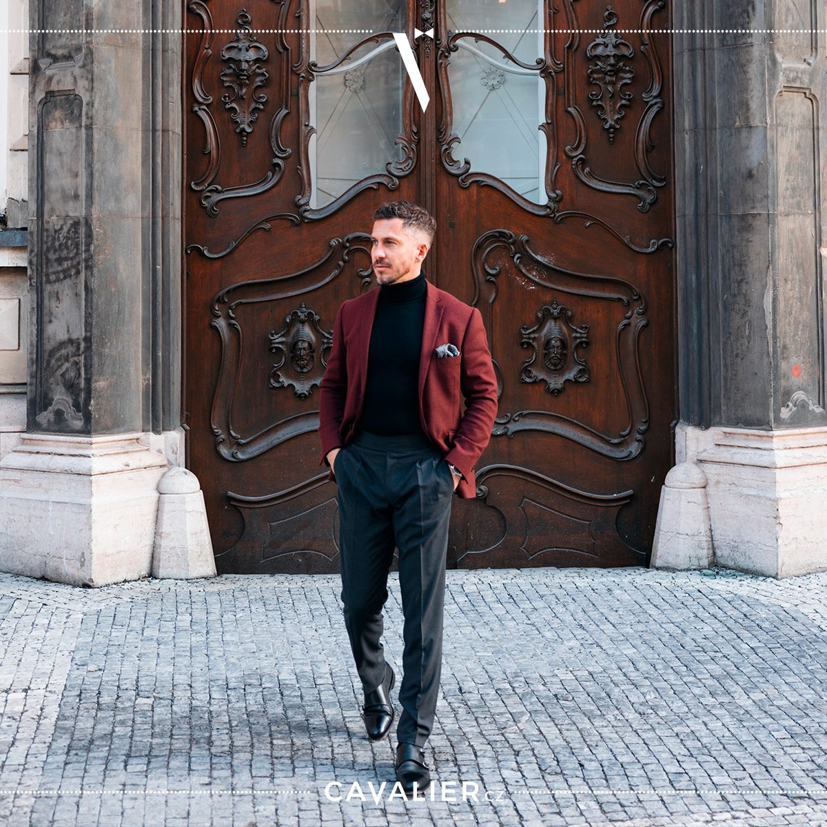 Muž v elegantním smart casual outfitu – vínové vlněné sako na míru Cavalier doplněné černým rolákem, tmavými kalhotami se faldy a koženými botami.