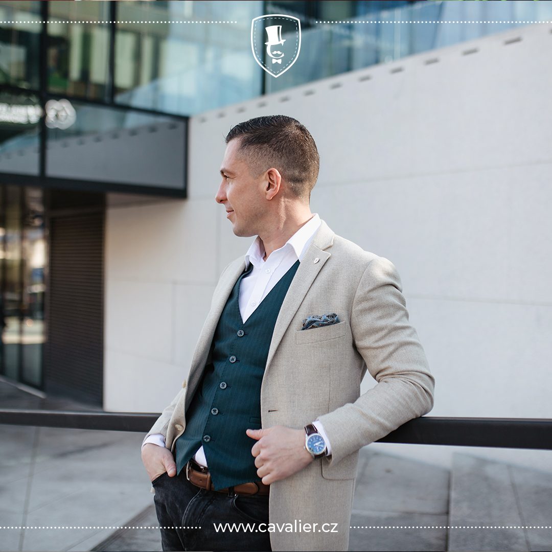 Muž v pánském smart casual outfitu – světlé strukturované sako na míru Cavalier doplněné tmavě zelenou vestou, bílou košilí s rozepnutým límcem a vreckovkou v náprsní kapsičce.