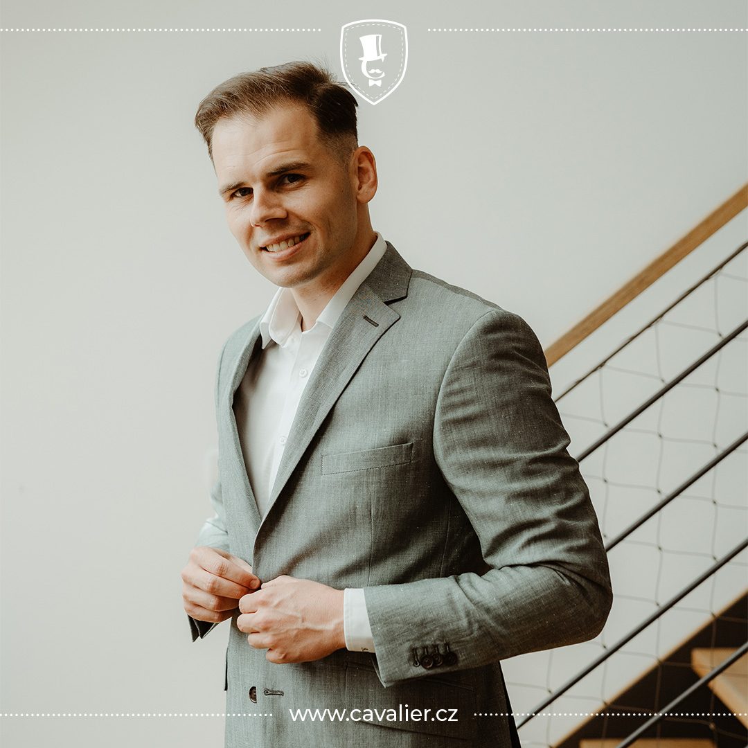 Usměvavý muž v lehkém šedozeleném saku na míru Cavalier a bílé košili jako inspirace pro výběr dokonalého svatebního obleku