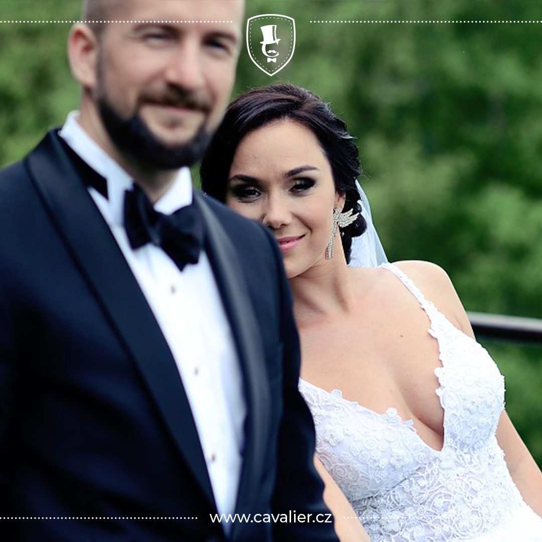 Ženich v elegantním černém smokingu na míru Cavalier se šálovým límcem a motýlkem po boku nevěsty jako ideální volba pro formální svatbu