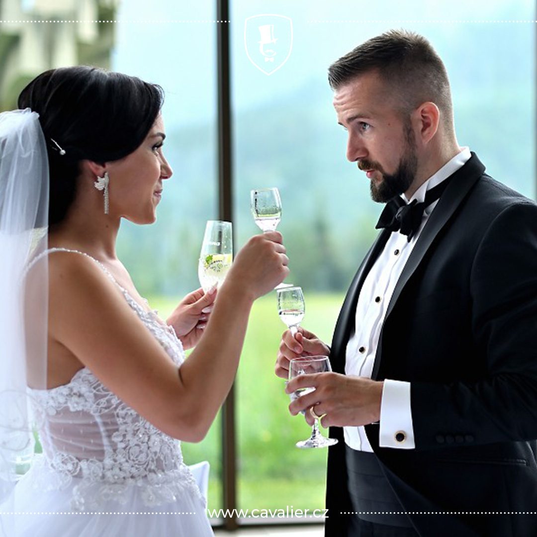 Novomanželé při slavnostním přípitku a ženich v černém smokingu na míru Cavalier s motýlkem a smokingovou košilí